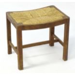 An early 20thC oak Heals stool with a bowed rush seat above four legs united by a H-stretcher. 20"