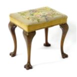 An early 20thC stool with a needlework top above four cabriole legs terminating in trifid feet.