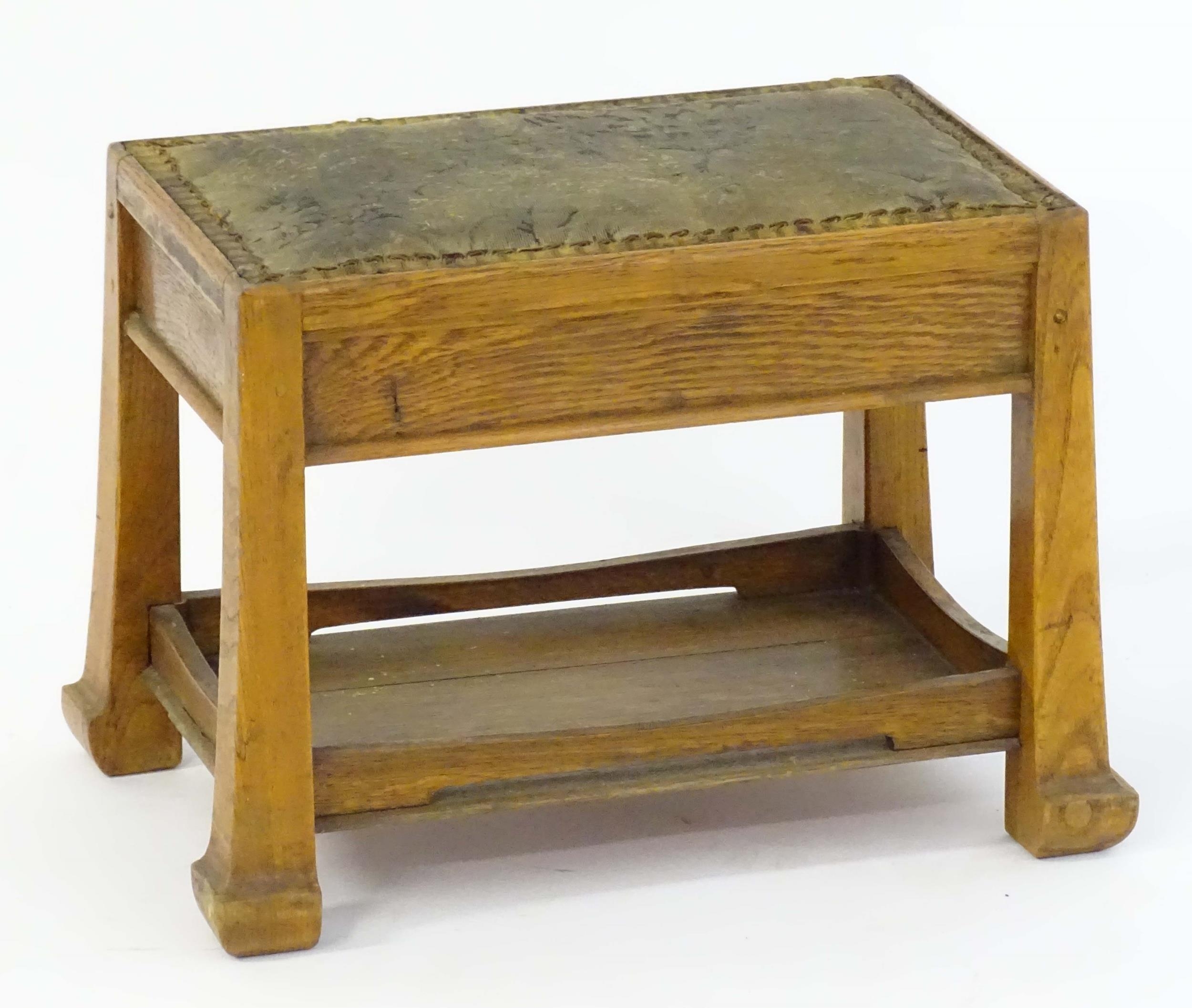 An Arts & Crafts oak footstool with an upholstered top above four tapering legs and an under tier