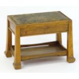 An Arts & Crafts oak footstool with an upholstered top above four tapering legs and an under tier