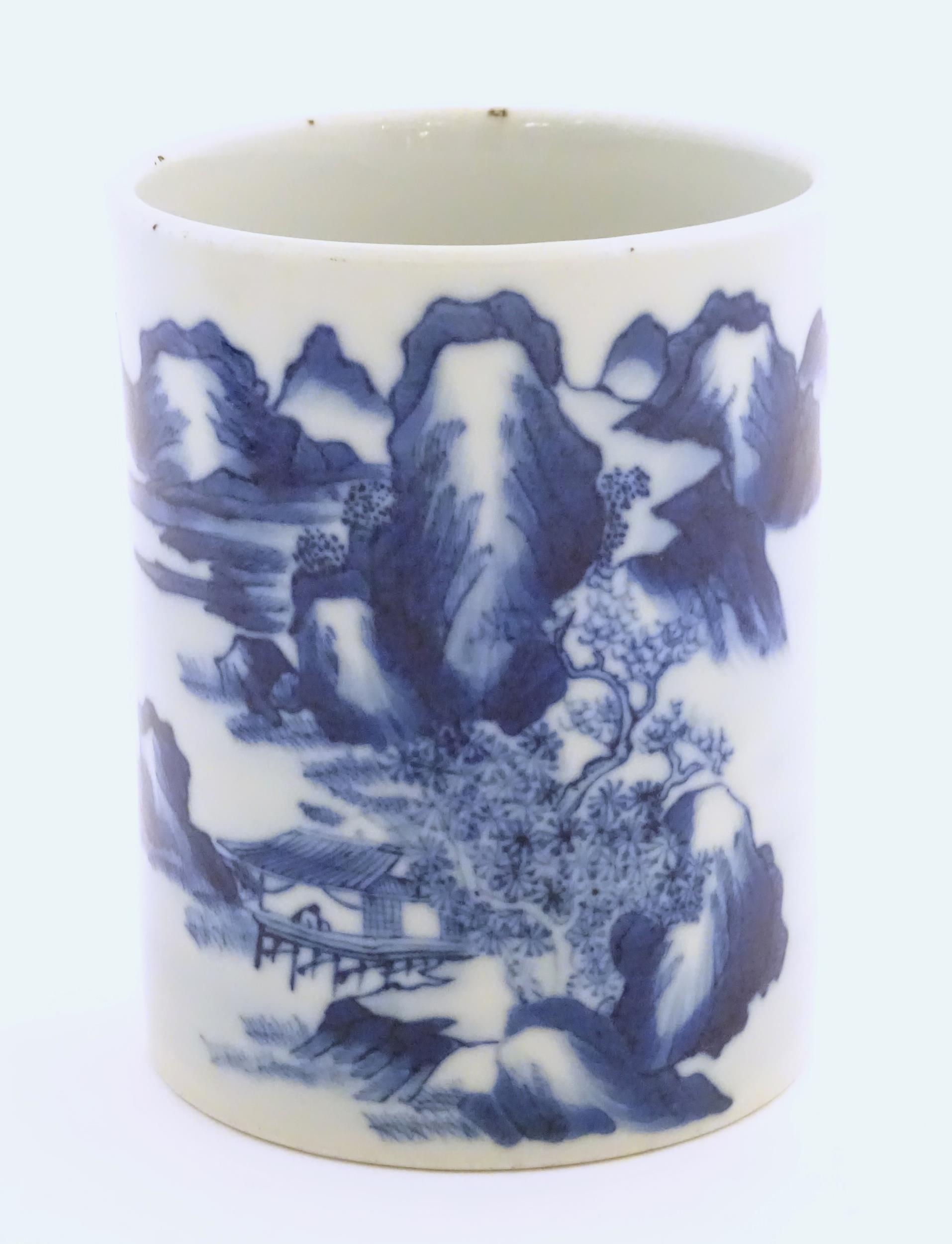 A Chinese blue and white brush pot of cylindrical form decorated with a stylised landscape with