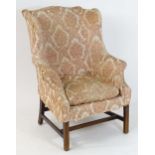 An 18thC wingback armchair with a shaped backrest, scrolled arms and raised on chamfered legs united