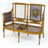An early 20thC satinwood bergere settee with a watercolour painted frame and panels, raised on