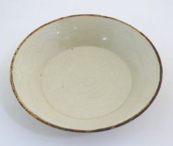 A Chinese Ding style dished plate with relief decoration depicting a stylised baby. Approx. 8"