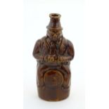 A Victorian treacle glazed spirit flask modelled as Old Tom, a man sat on a barrel with a jug and