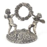 A Continental white metal table / place card holder formed as cherubs/ cupids holding a flower