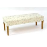 A 20thC footstool with floral upholstery and standing on four tapering legs. 48" long x 19" wide x