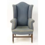 A 19thC wingback armchair with a shaped top above scrolled arms and a sprung seat, standing on