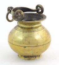 A brass water pot with bulbous body and swing handle with hanging loop and incised banded