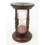 An early 20thC hourglass / sand timer with turned wooden ends supported by four turned treen