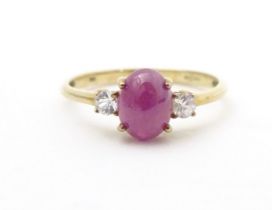 A 9ct gold ring with ruby coloured cabochon flanked by two white stones. Ring size approx. N 1/2