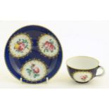 A Continental cup and saucer the blue ground decorated with hand painted panels depicting floral