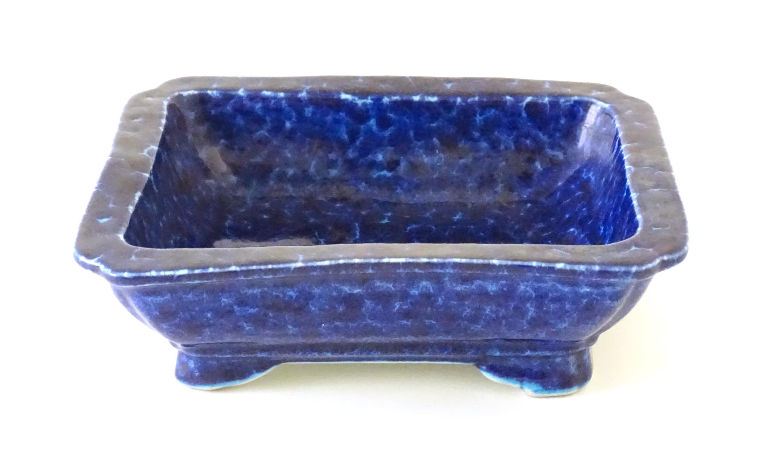 A Chinese dish of rectangular form with a blue glaze, raised on four feet. Character marks under.
