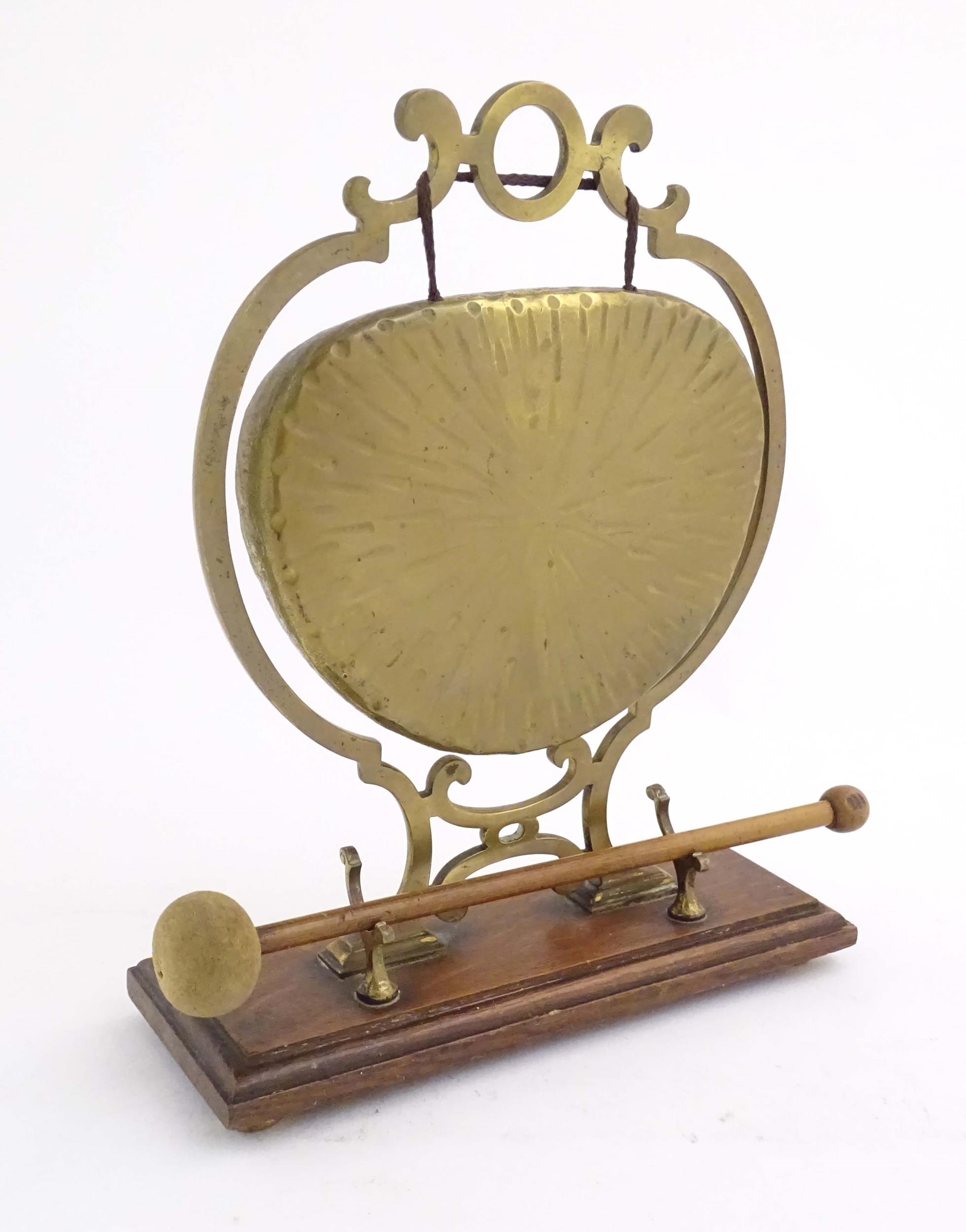 A 20thC brass table gong within a scrolling brass surround, on a rectangular oak base with beater.