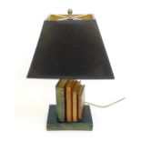 A novelty table lamp, the ceramic base formed as piled books and supporting a single column,