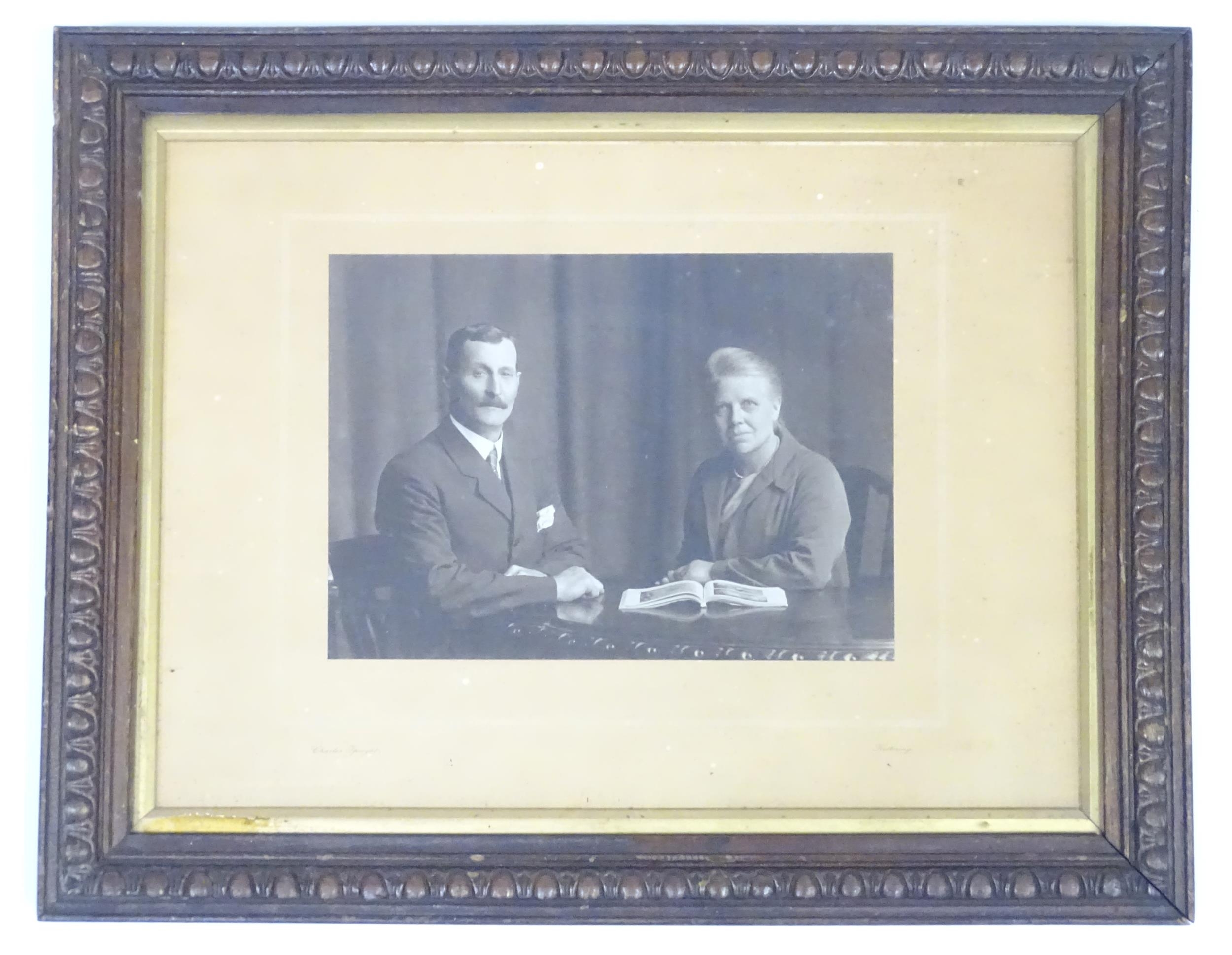 An early 20thC monochrome photograph depicting a man and a woman seated at a table with an open