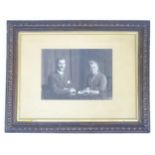 An early 20thC monochrome photograph depicting a man and a woman seated at a table with an open