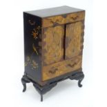 An oriental black lacquered cabinet with carrying handles to the side and resting on a stand. The