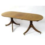 An early 20thC mahogany dining table of narrow form with a reeded edge and double pedestal base,