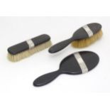 A three piece dressing table set, comprising hand mirror and two brushes with ebonised handles and