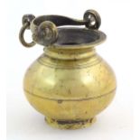 A brass water pot with bulbous body and swing handle with hanging loop and incised banded