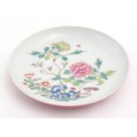 A small Chinese famille rose plate decorated with a stylised rocky outcrop with flowers and foliage.