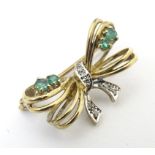 A 9ct gold brooch of bow form set with diamonds and emeralds. 1" wide Please Note - we do not make