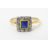 A gold ring set with central sapphire bordered by diamonds in a square setting. Ring size Approx L