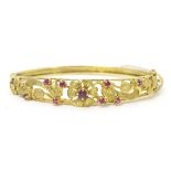 A 9ct gold bangle bracelet with floral and foliate detail set with rubies. Please Note - we do not