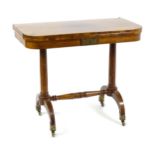 A Regency period rosewood card table of D-form, having a brass inlaid top revolving and opening to