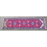 Carpet / Rug : A red ground runner with central motifs and geometric border. Approx 118" x 30 1/2"