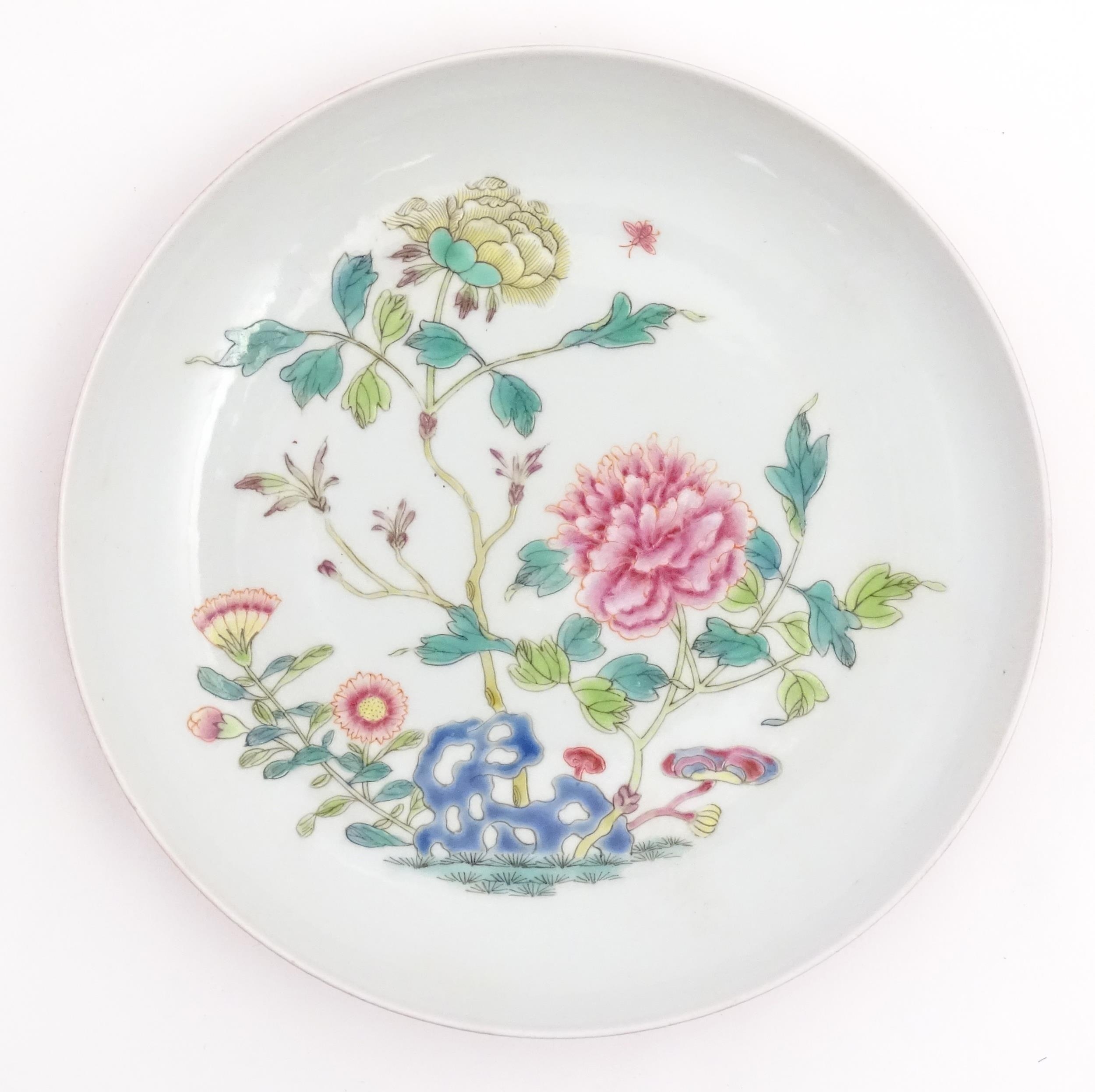 A small Chinese famille rose plate decorated with a stylised rocky outcrop with flowers and foliage.