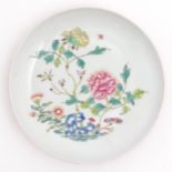 A small Chinese famille rose plate decorated with a stylised rocky outcrop with flowers and foliage.