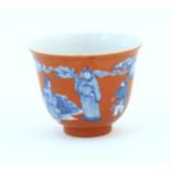 A Chinese tea bowl with a red ground decorated in blue with figures in a landscape. Character