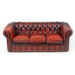 A late 20thC red leather Chesterfield sofa with deep buttoned upholstery and scrolled arms with