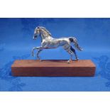 A SILVER HORSE MOUNTED ON A WOODEN BLOCK