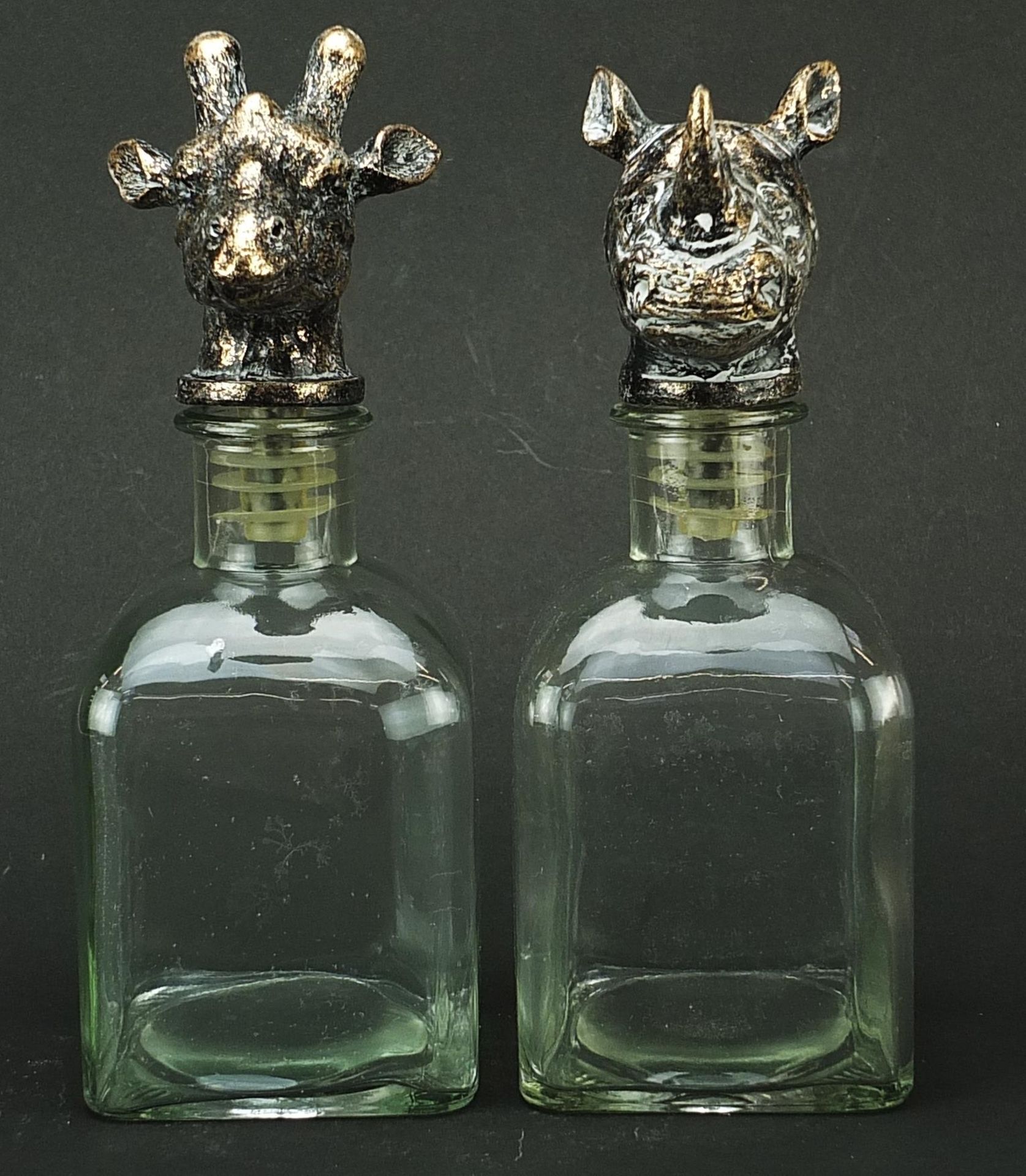 Pair of glass decanters with bronzed rhinoceros and giraffe head stoppers, 24cm high Both appear