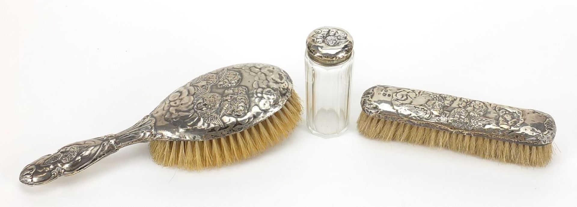 Two silver mounted brushes and a cut glass jar, each embossed with Putti, various Birmingham