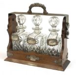 Silver plated and oak three bottle tantalus with three glass decanters and three decanter labels,