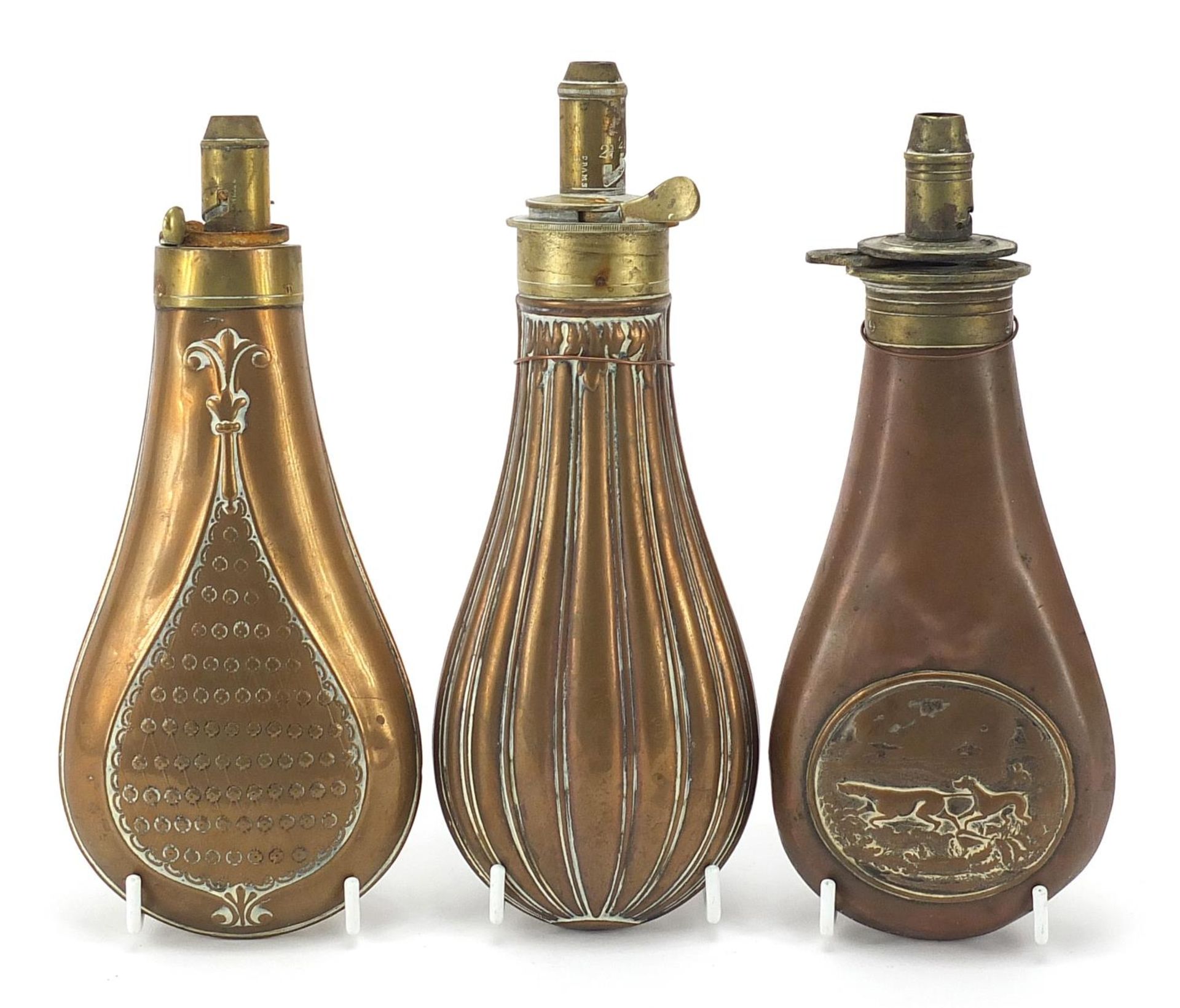 Three 19th century copper and brass powder flasks including one embossed with two hounds,