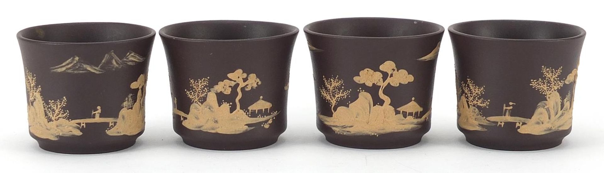 Four Chinese Yixing terracotta cups hand painted with landscapes, impressed character marks to the