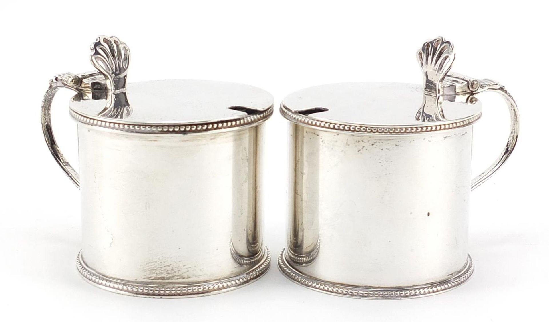 Sydney Bellamy Harman, pair of George V silver mustards with hinged lids and blue glass liners,