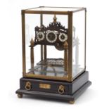 Brass Congreve style rolling ball clock with three enamel dials housed in a glazed display case