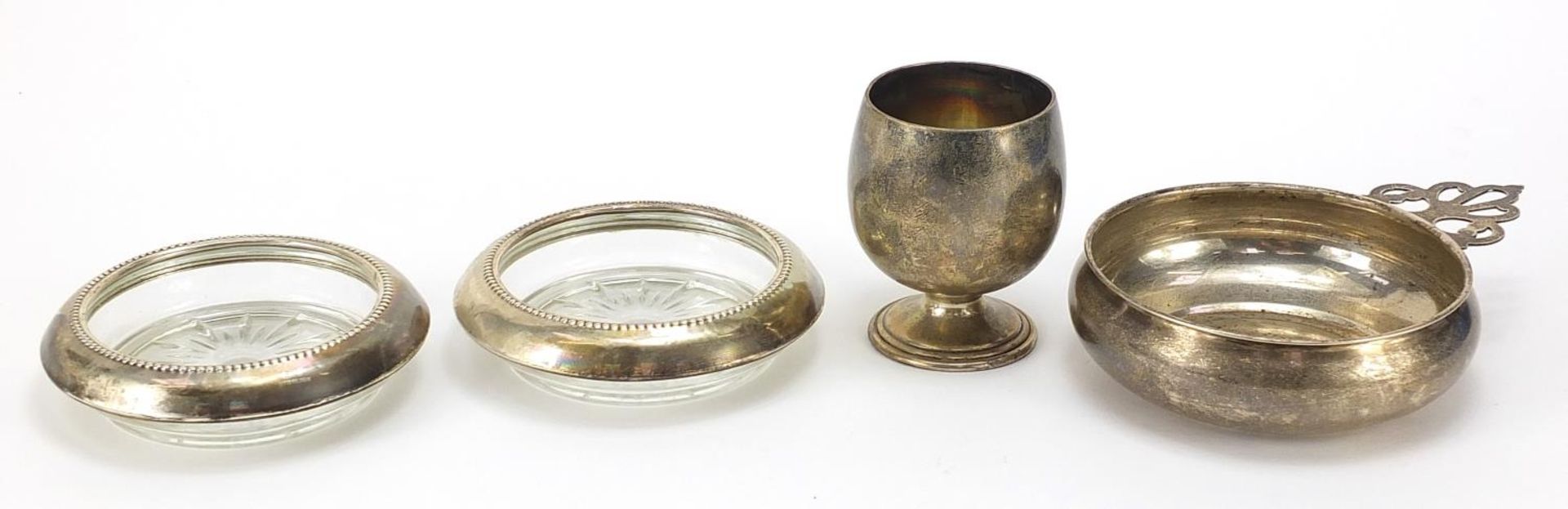 Sterling silver porringer, egg cup and pair of glass coasters with silver mounts, the largest 14cm