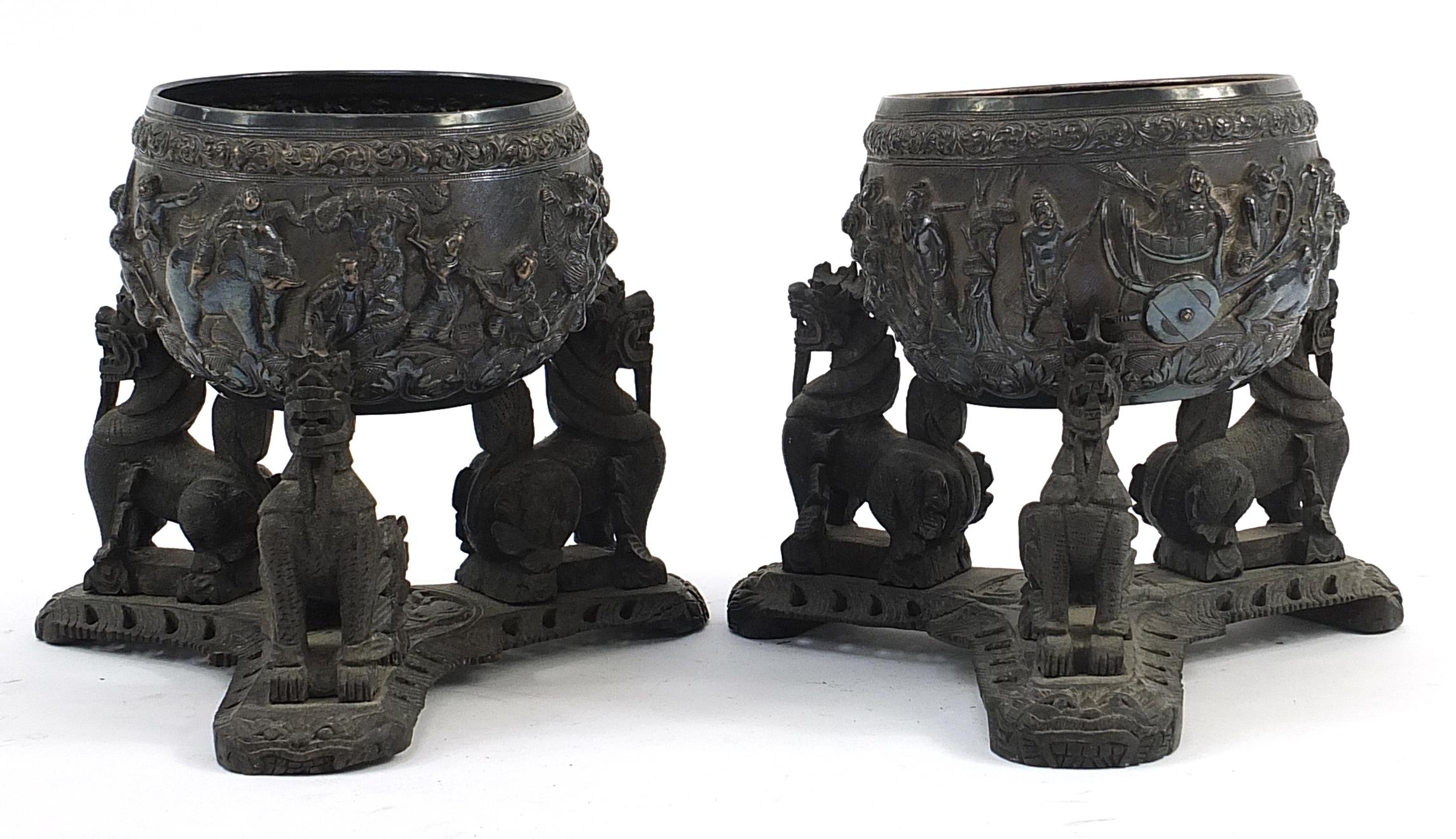 Pair of Burmese unmarked silver bowls embossed with figures raised on hardwood stands, each bowl