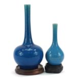 Two Chinese porcelain long neck bottle vases having blue glazes raised on hardwood stands, the