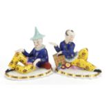 Pair of English porcelain figures of resting Chinese boys, each 14cm wide