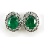 Pair of 18ct white gold oval emerald and diamond cluster stud earrings, total emerald weight