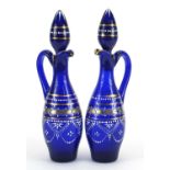 Pair of blue glass oil and vinegar bottles hand painted with flowers, each 28cm high