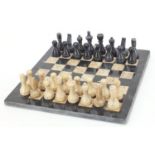 Carved stone chess set with inlaid marble board, the largest pieces each 6.5cm high, the board